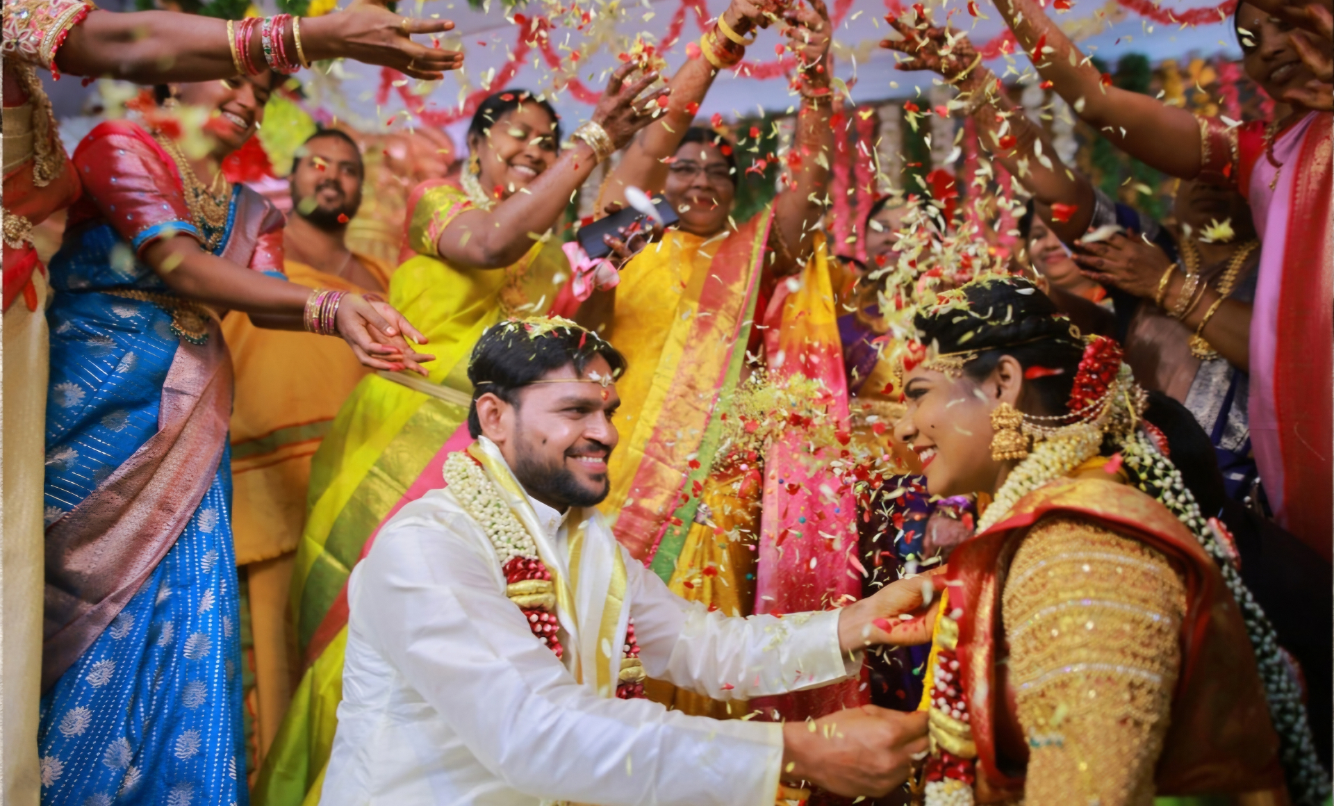 Bride and groom seated as family showers flower petals during a traditional South Indian wedding blessing