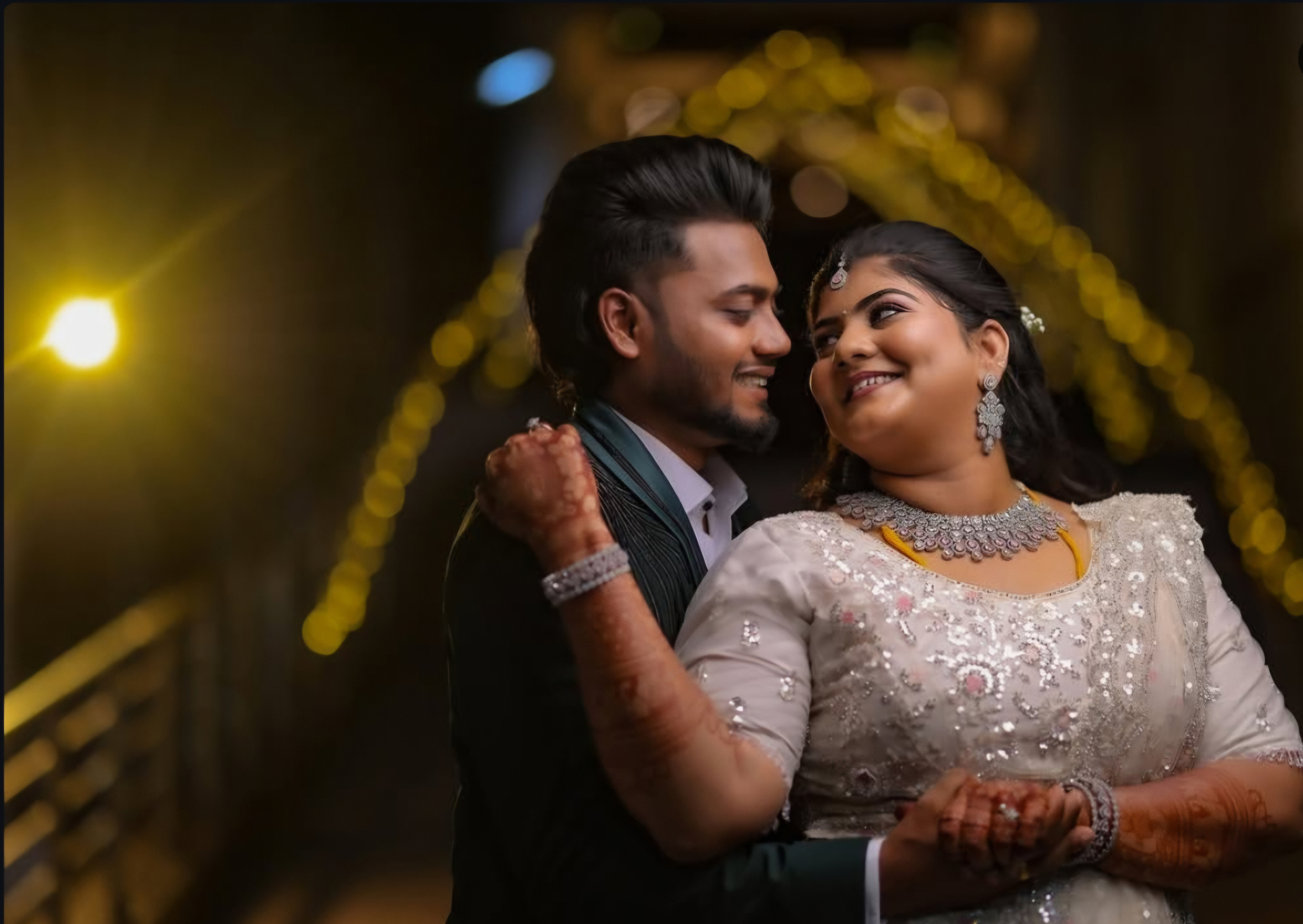 Couple smiling at each other under warm bokeh string lights at an evening wedding reception