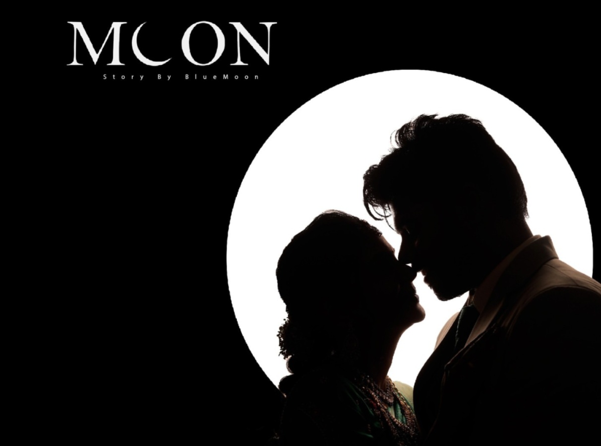 Silhouetted couple facing each other in front of a large full moon on a black background with the word MOON